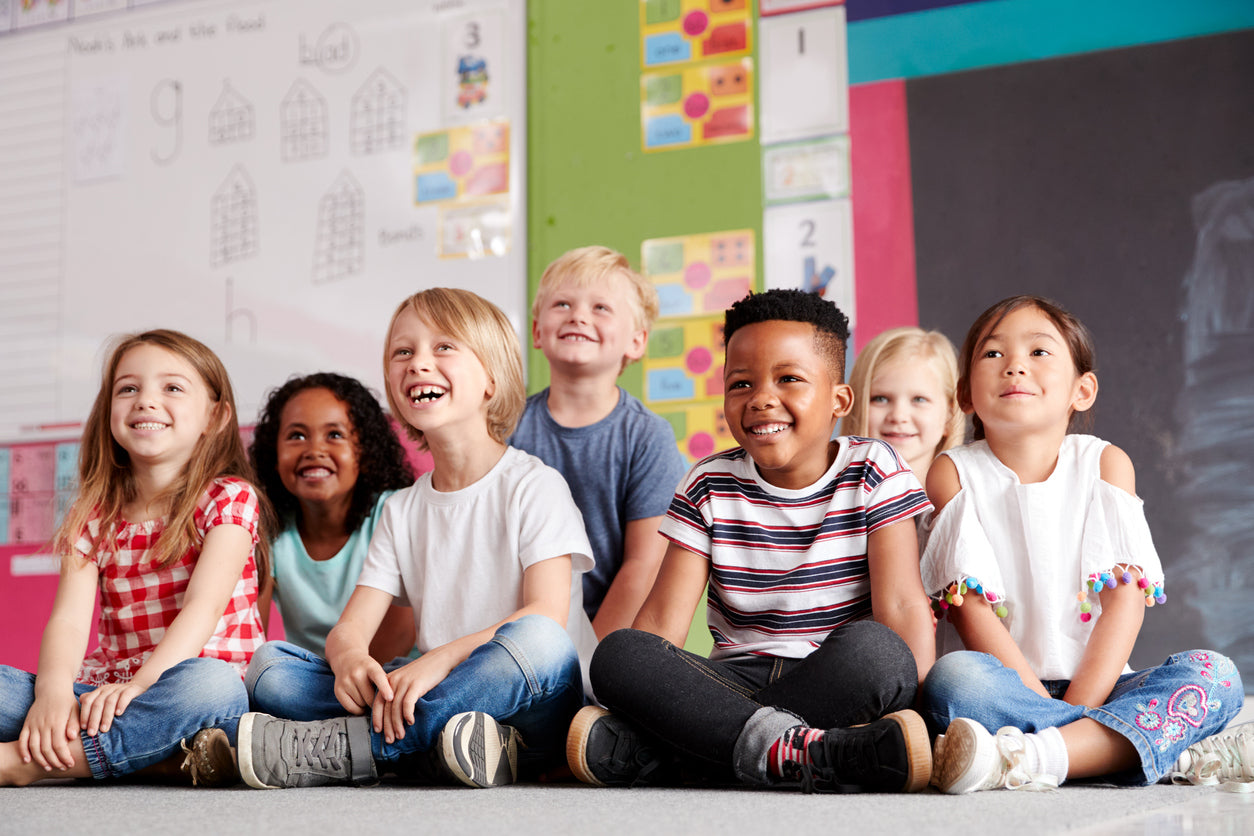 group of elementary school students smiling sitting on the floor in the classroom