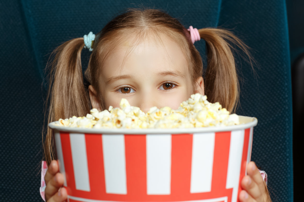 little girl peaking out from behind a big bucket of popcorn 