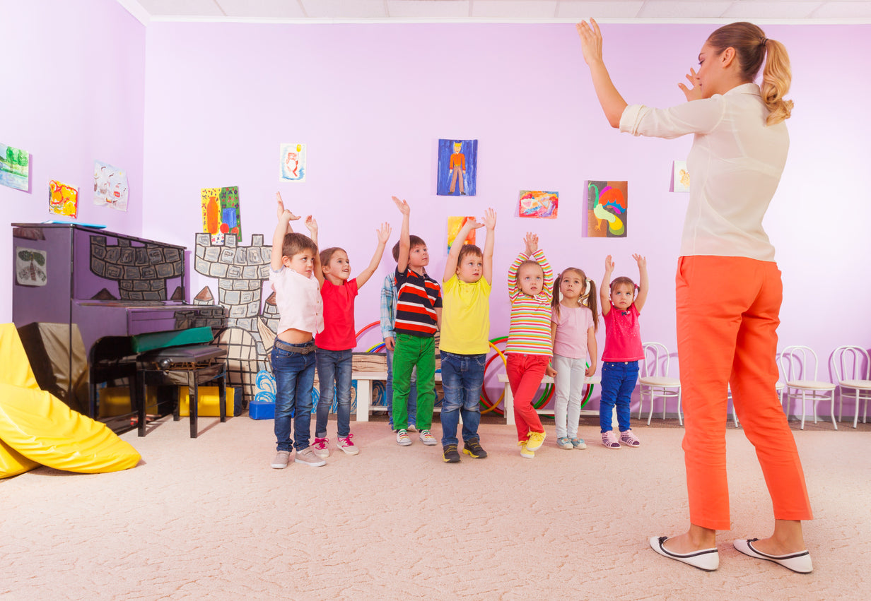 teacher and young students with their arms in the air in the classroom